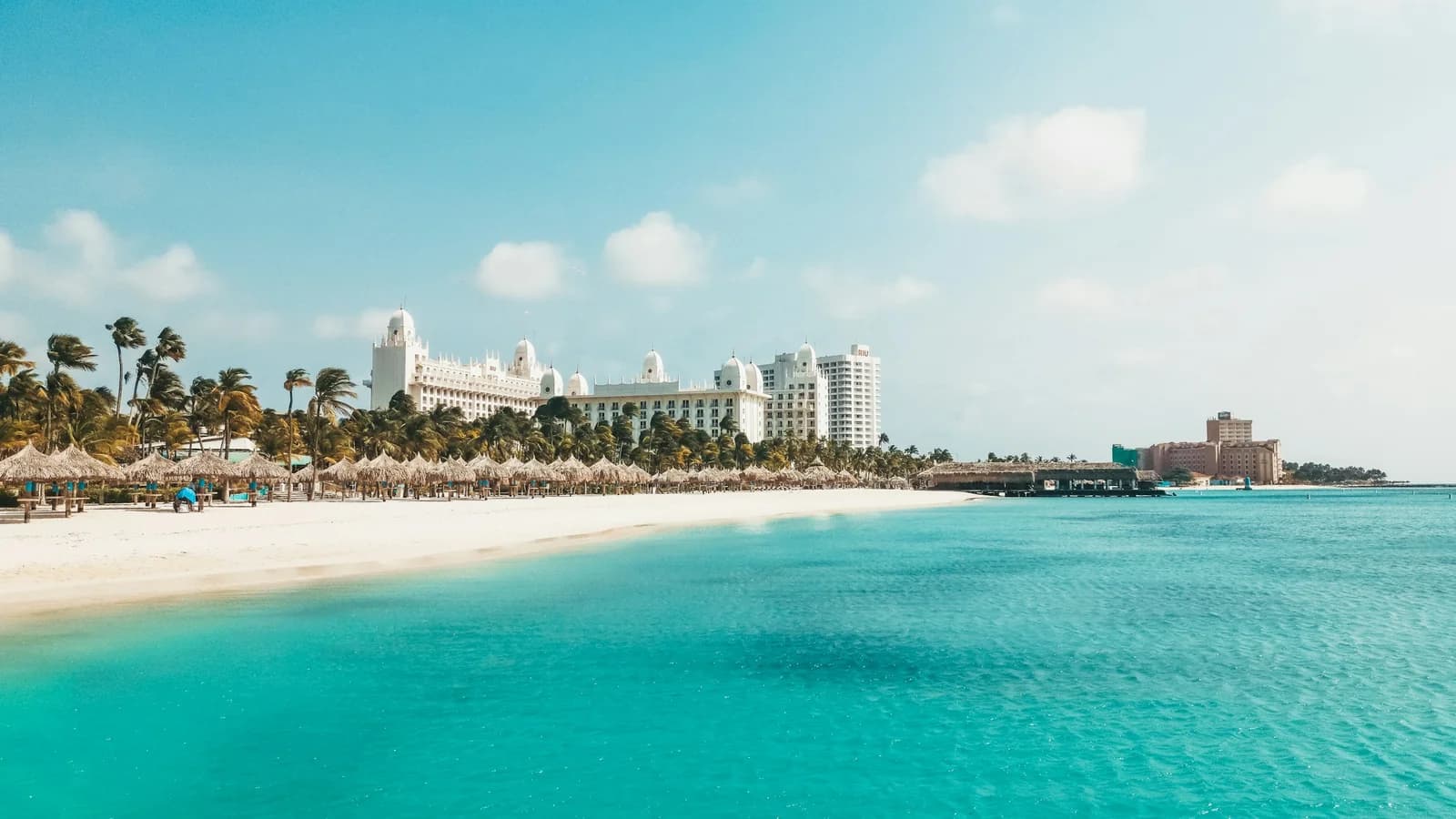 White-sand beach in Aruba with a resort hotel in the background under a clear sky
