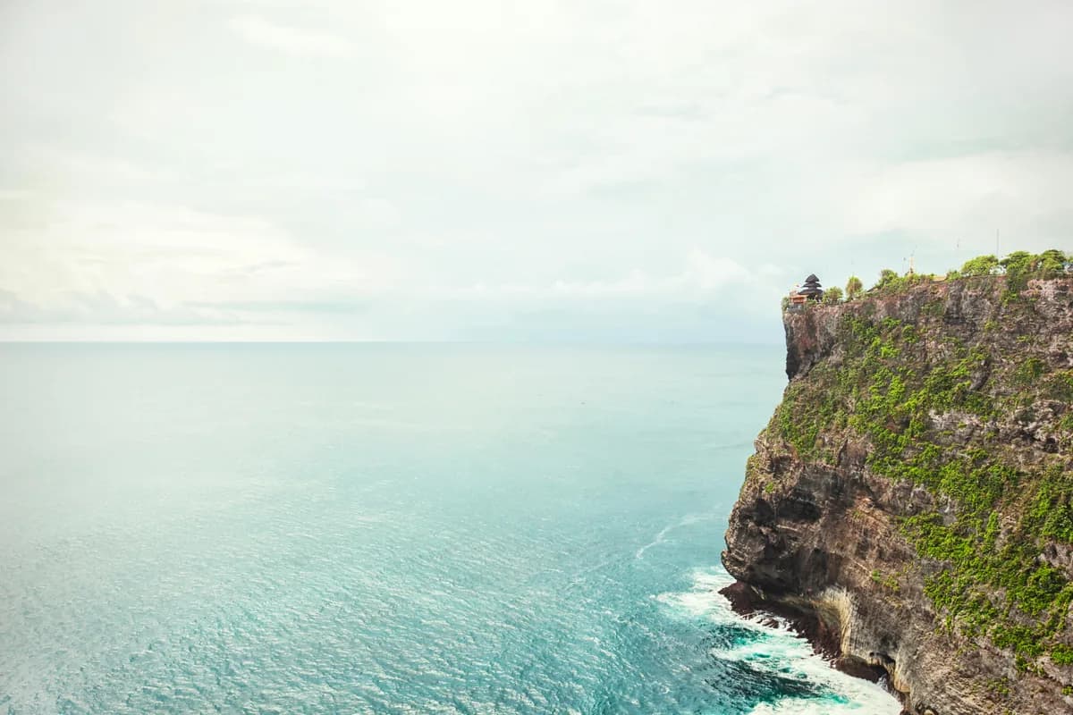 Stunning view of Uluwatu cliffs meeting the blue ocean in Bali, Indonesia, under a bright summer sky.