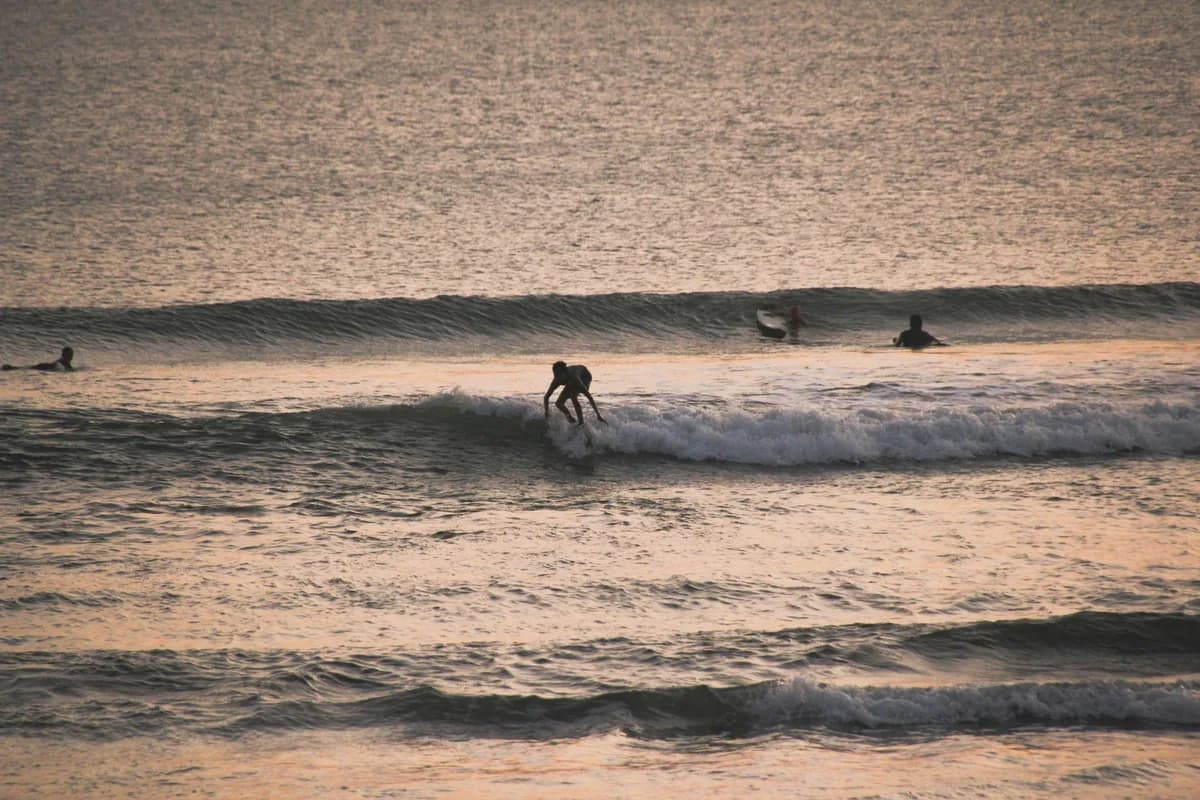 A surfer rides the waves during a stunning sunset on a Bali beach, showcasing water sports excitement.