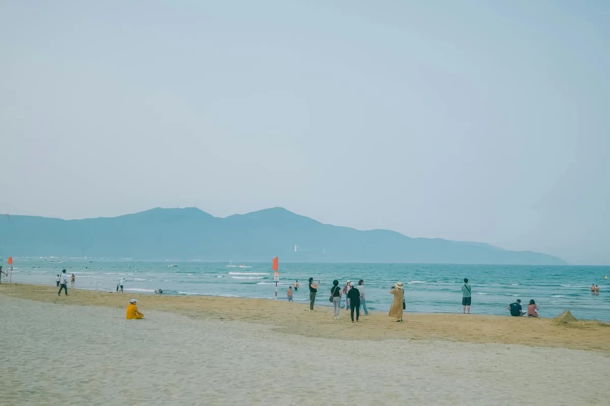 A serene beach in Vietnam with visitors enjoying the coastal scenery and distant mountains.
