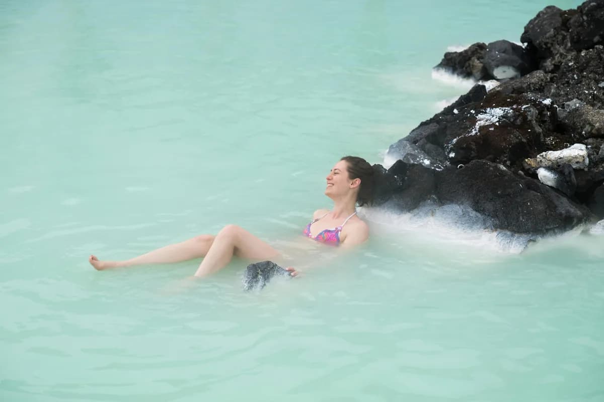 Person enjoying a serene moment in Iceland's geothermal waters, surrounded by volcanic rocks.