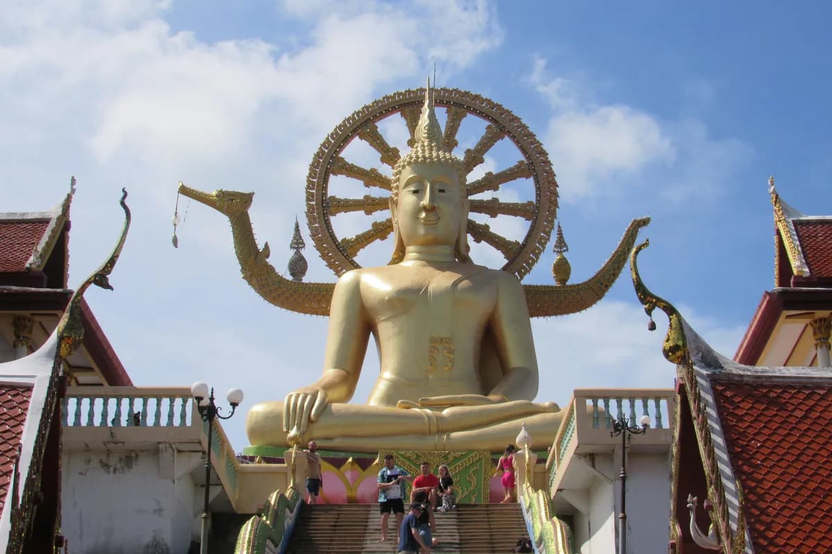Majestic golden Buddha statue at Wat Phra Yai temple, Thailand, showcasing vibrant cultural architecture.