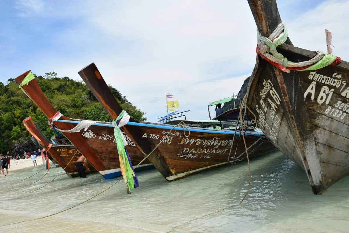 Long-tail boats anchored on a picturesque tropical beach with clear water and green hills.