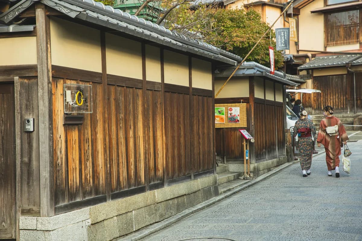 Japanese ladies in traditional kimonos walking on a paved street near aged wooden houses in the Gion district of Kyoto.