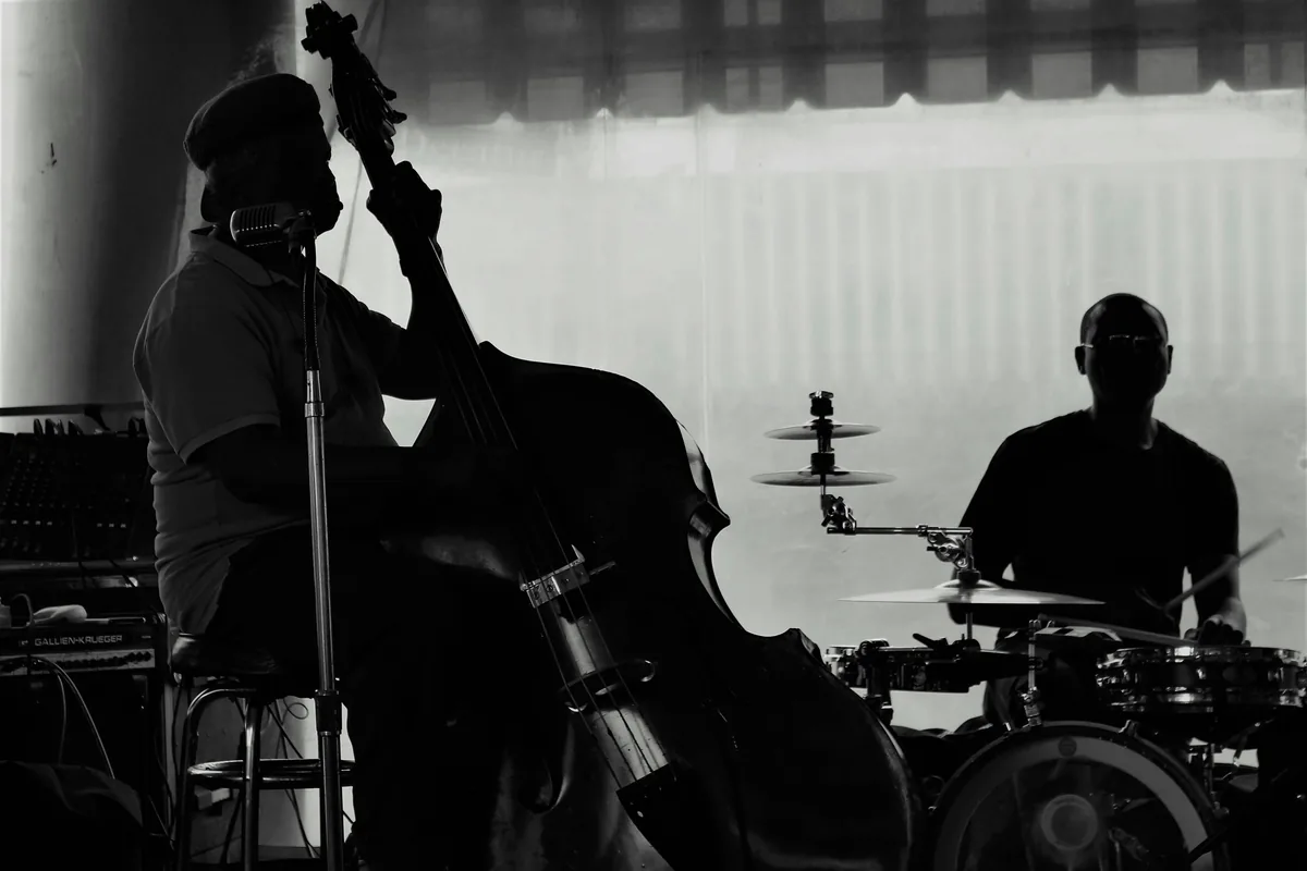 Silhouette of bass and drum musicians performing live jazz music in a dim venue.
