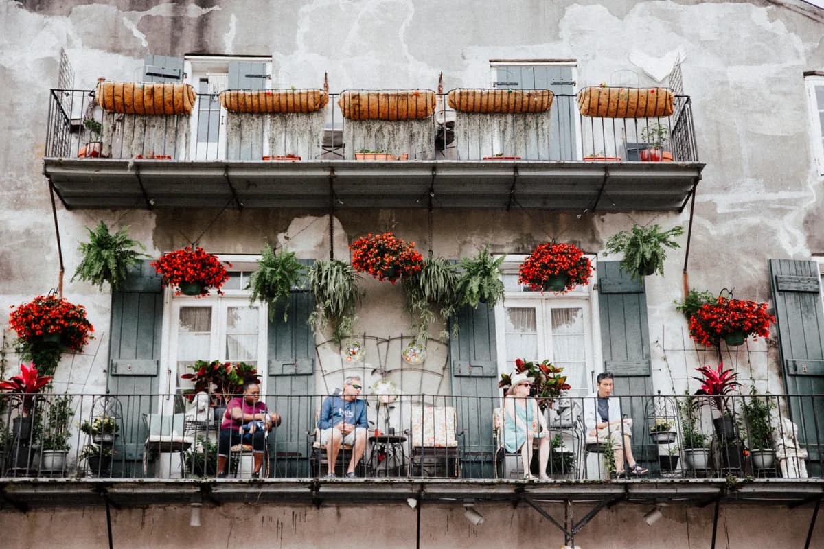 A picturesque New Orleans balcony scene with people relaxing and colorful floral decorations in the French Quarter.