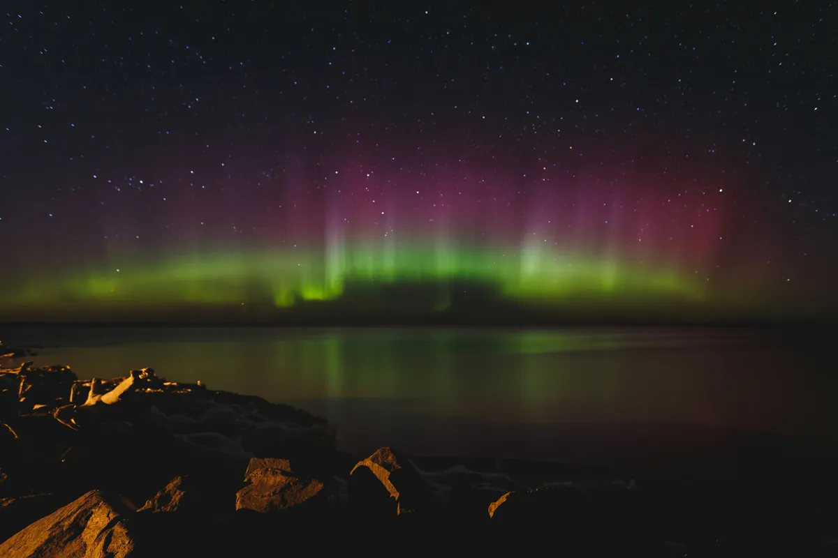 Green and red aurora over the water from a rocky shore near Ironwood, in Michigan’s western Upper Peninsula
