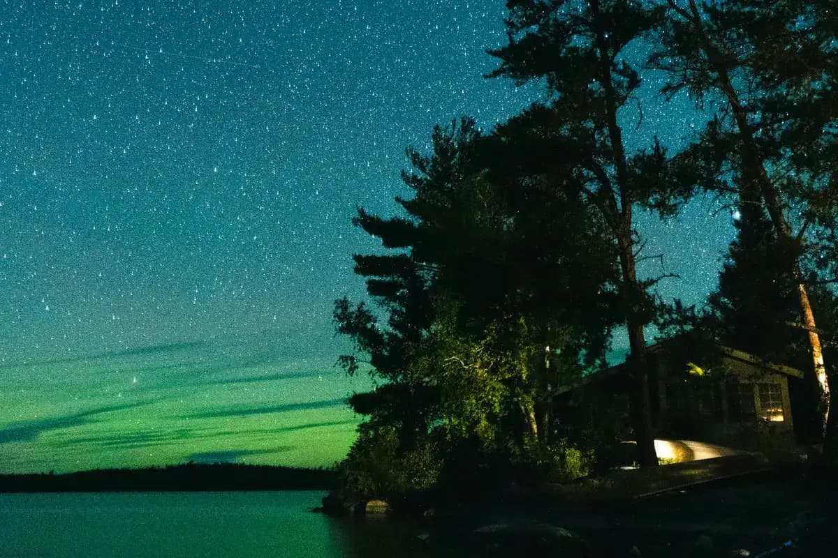 Green aurora low over a lake beside a lakeshore cabin and pines near Ely, Minnesota