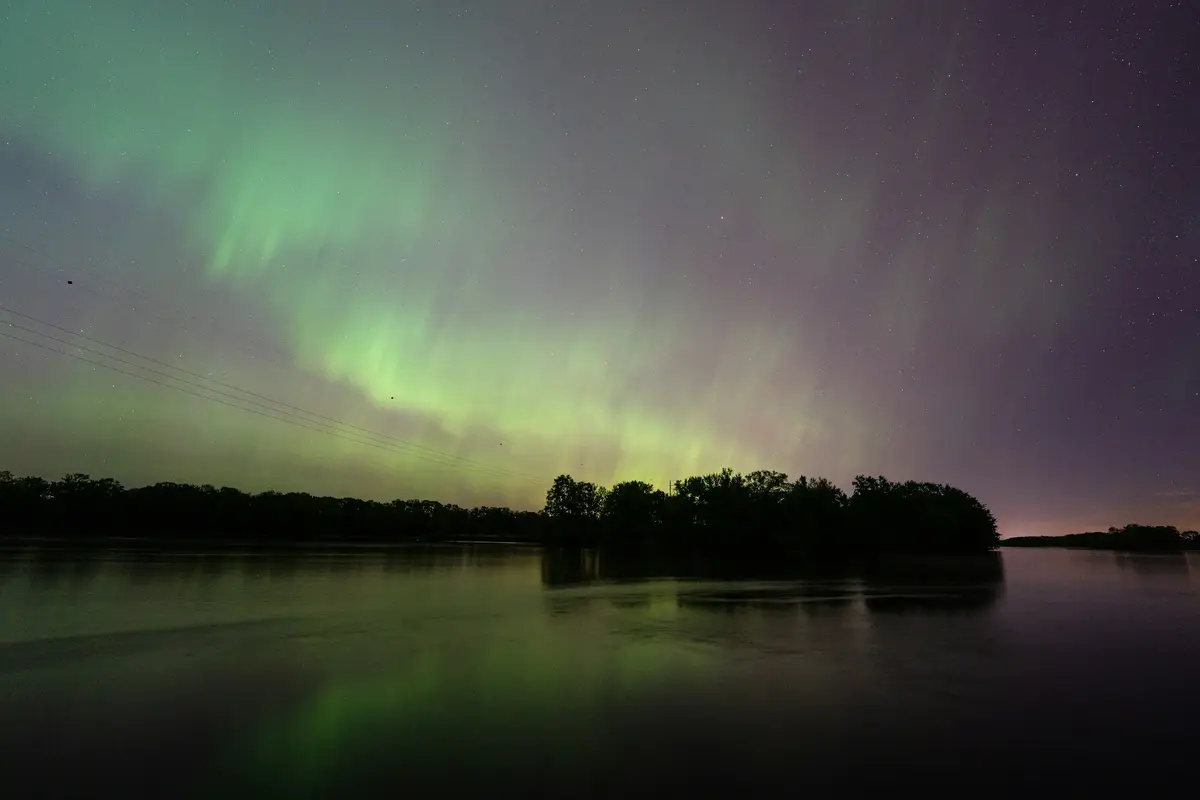 Green aurora above a tree line, reflected in a still lake near Madison, Wisconsin