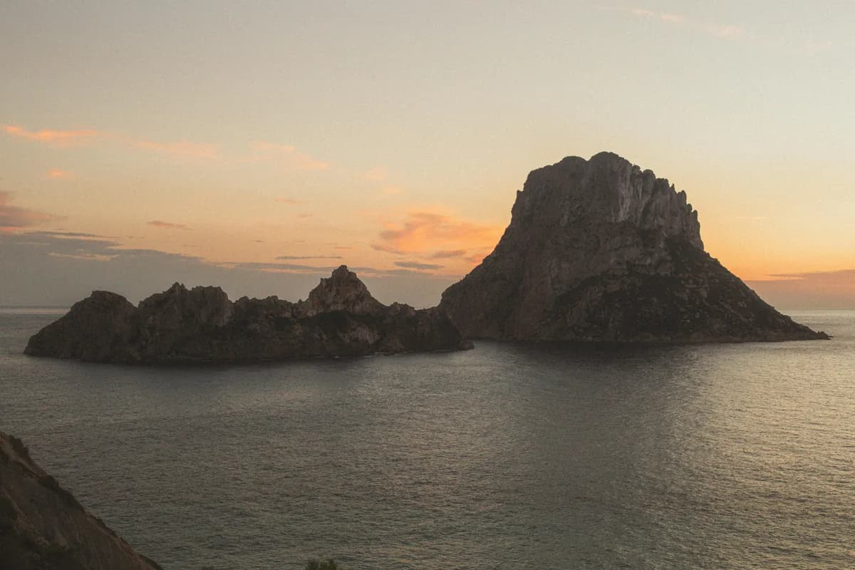 Stunning sunset view of the Es Vedrà island in Ibiza, Spain with calm waters and vibrant skies.