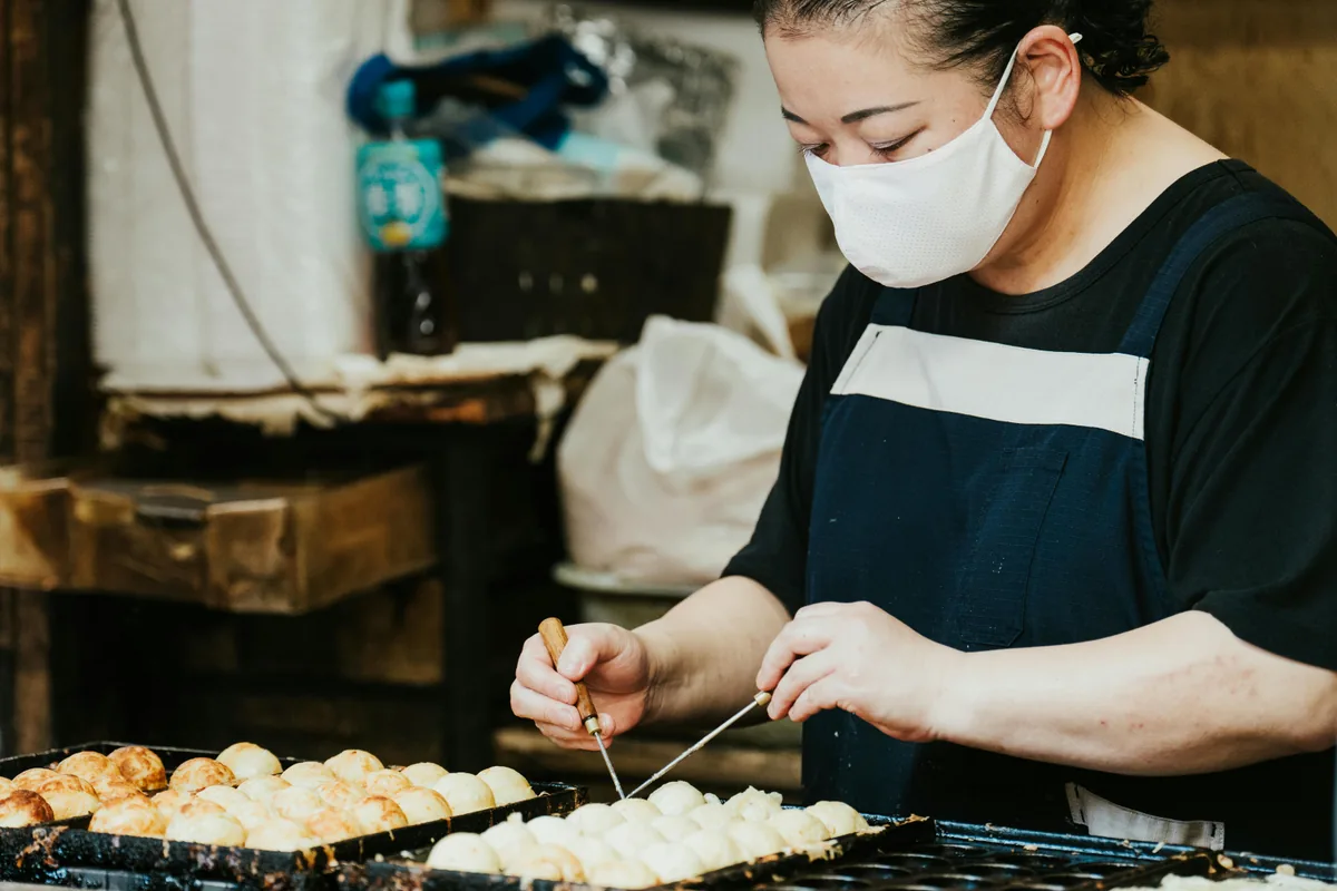 A Japanese street food vendor skillfully preparing takoyaki at an outdoor market in Japan.