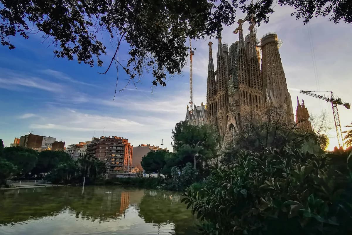 The iconic Sagrada Familia in Barcelona at sunset with reflections on a nearby pond.
