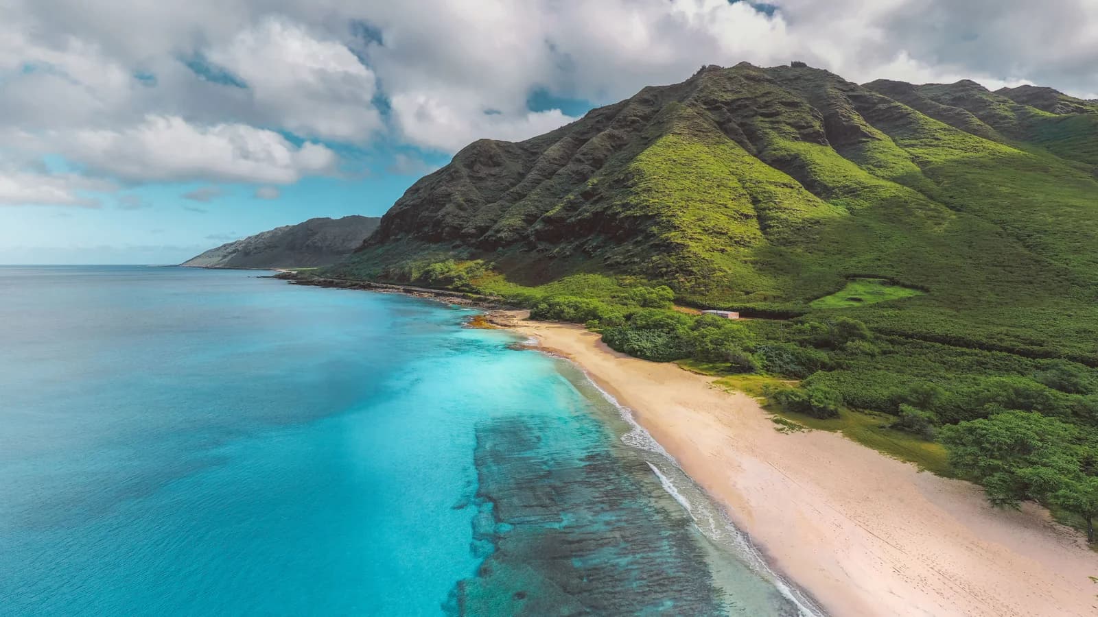 Aerial view of a Hawaiian coastline with green mountains meeting clear turquoise water