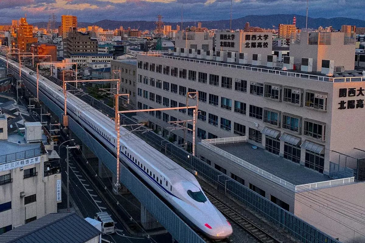 A white bullet train on an elevated line through the city at sunset