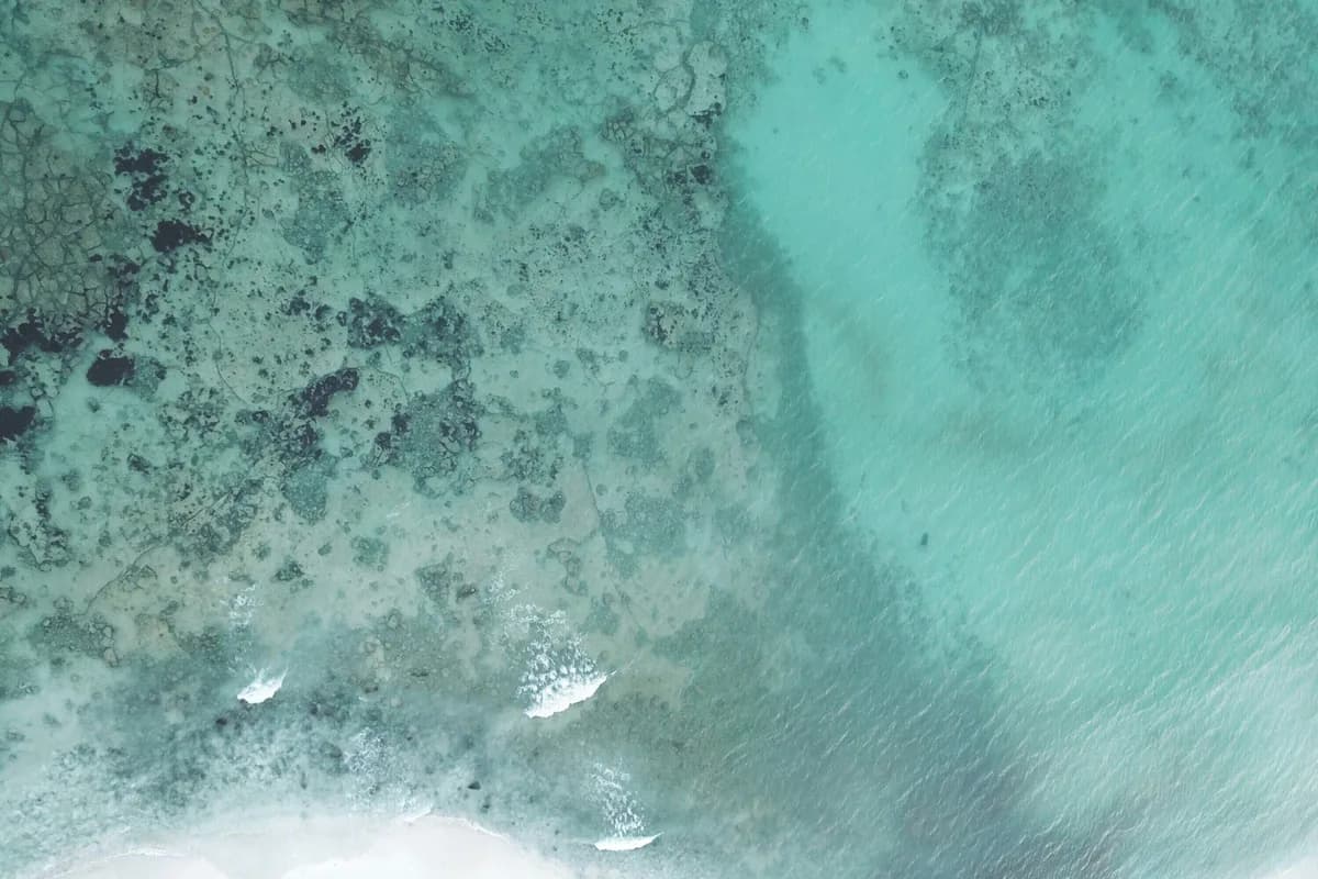 Turquoise Caribbean water and reef from above, with a strip of white sand along the shore