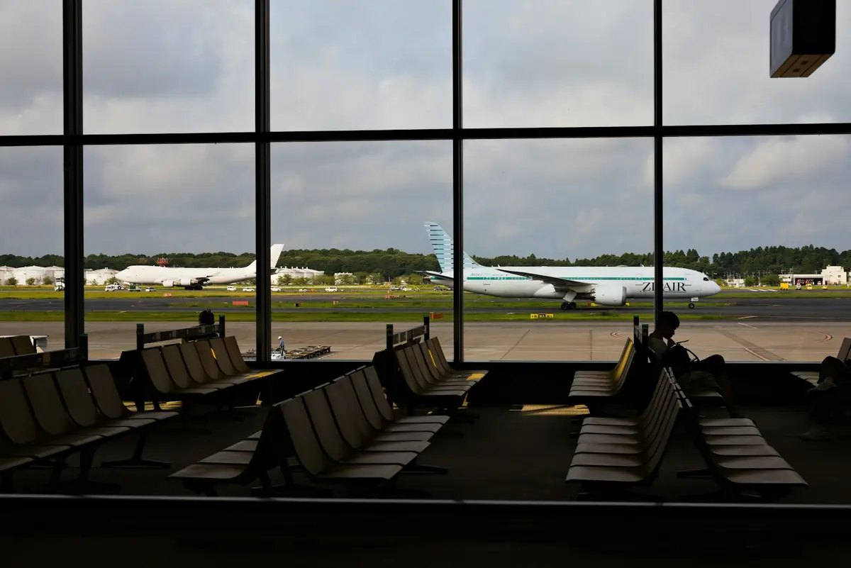 An airport departure lounge with tall windows looking out over parked planes