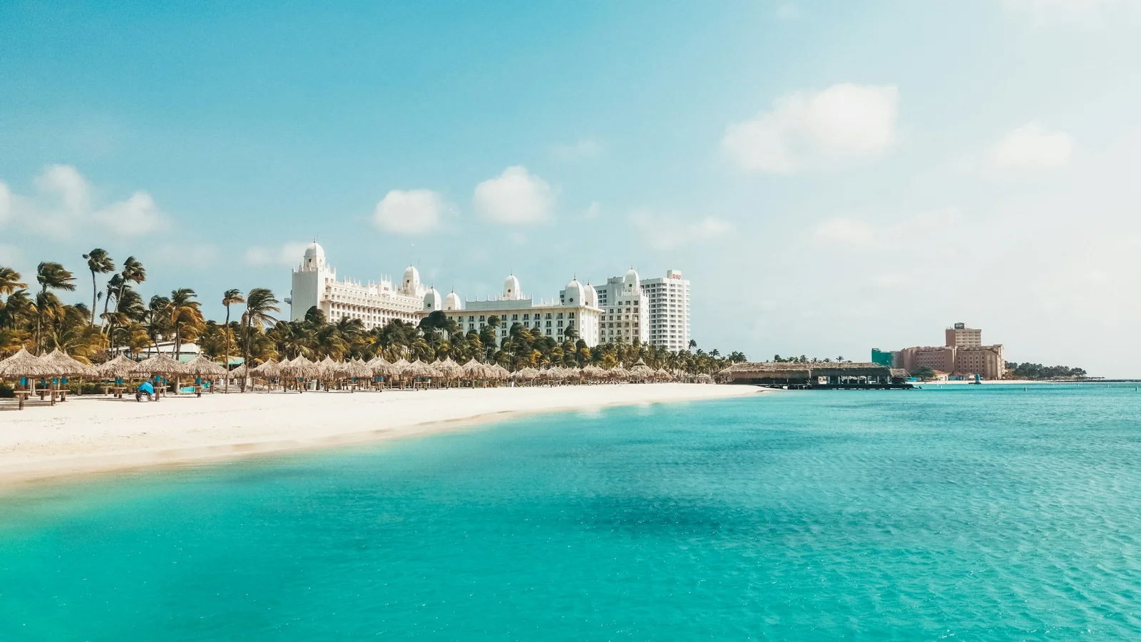 White-sand beach in Aruba with a resort hotel in the background under a clear sky