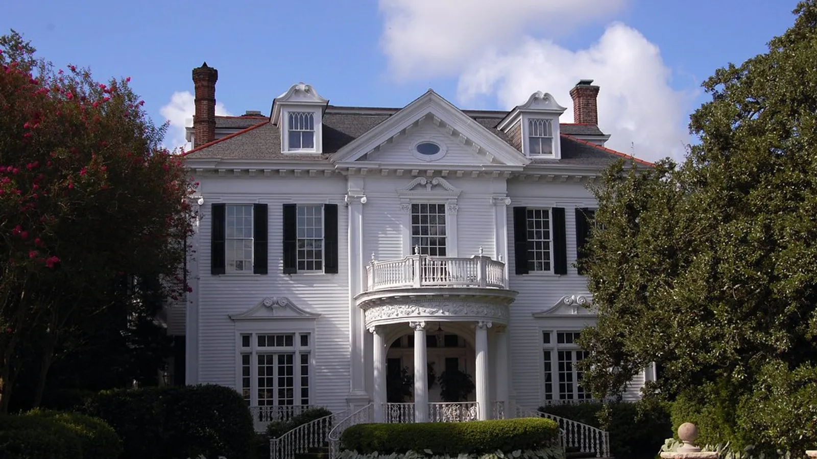 Stately Greek Revival mansion in the New Orleans Garden District — white columns, wraparound porch, oak-shaded grounds